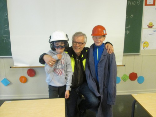 Ivar Hartviksen og to gutter, -en med ny hjelm med hørselvern og vernebriller og en med gammel jernverksfrakk og besøkshjelm.